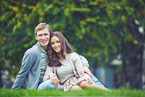 Young lovely couple sitting on grass outdoors
