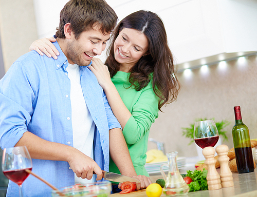 Happy woman embracing her husband while he cooking salad