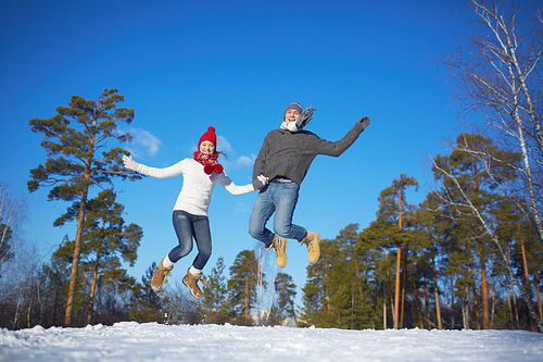 Young valentines in knitted clothes jumping in winter park or forest
