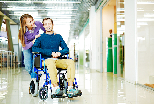 Full color image of young couple, handicapped man in wheelchair and his girlfriend, enjoying leisure time at shopping center together