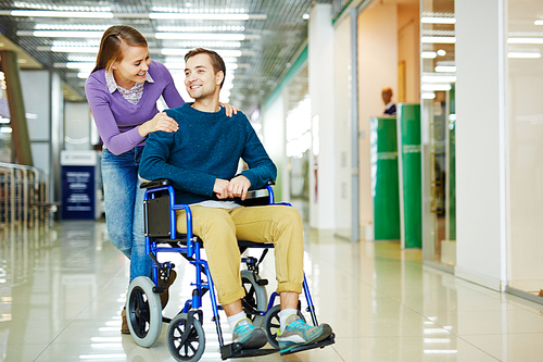 Young couple, woman and physically impaired man in wheelchair, having fun as they stroll in shopping center together dressed in colorful clothes