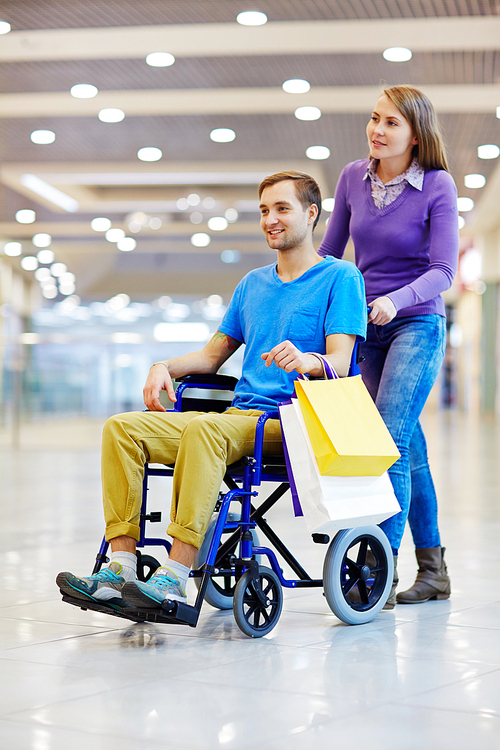 Modern girl and her boyfriend on wheelchair visiting shopping center