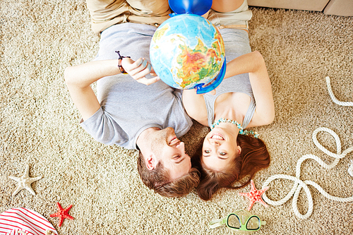 Restful young couple with globe lying on the floor at home
