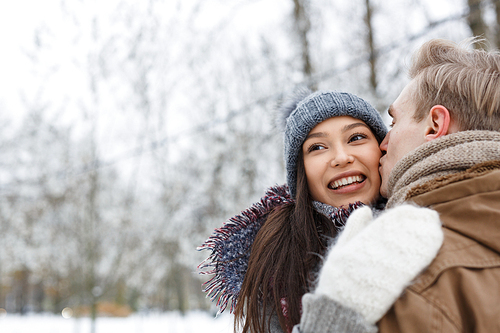 Boyfriend kissing happy girl on cheek outdoors