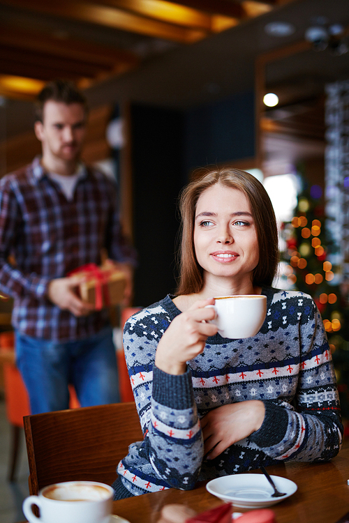Pretty young woman having coffee while her boyfriend going to make her xmas surprise