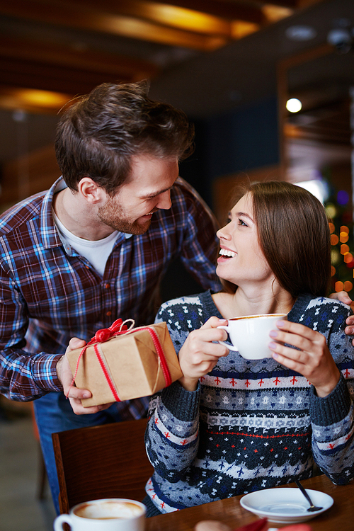 Surprised girl with cup of coffee looking at her boyfriend with xmas gift