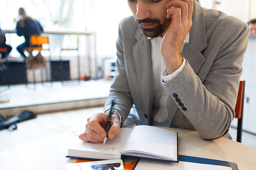 Man writing in notebook while talking on cellphone at work