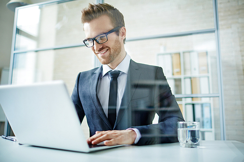 Smiling businessman wearing eyeglasses using his laptop at workplace