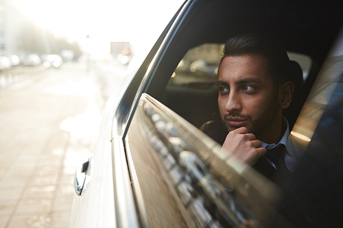 Wealthy man looking through car window while traveling in the city
