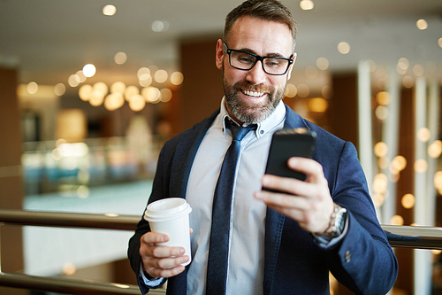 Contemporary employee with coffee reading sms
