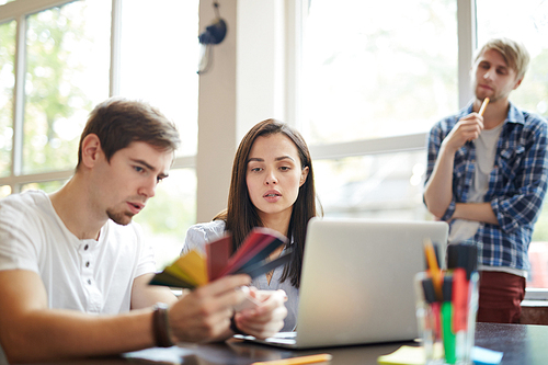 Young designer looking at palette held by co-worker during discussion