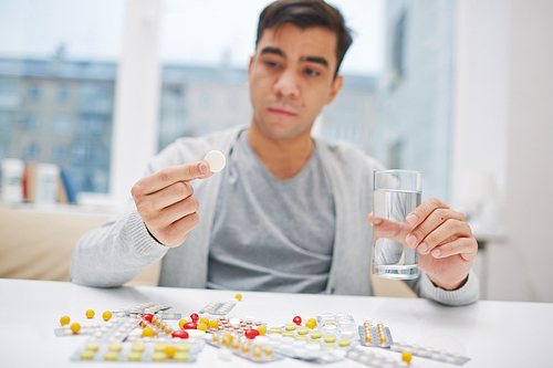 Young man sitting at the table and taking a pill
