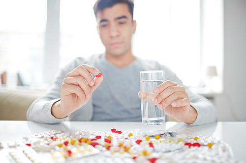 Young man holding pill and a glass of water