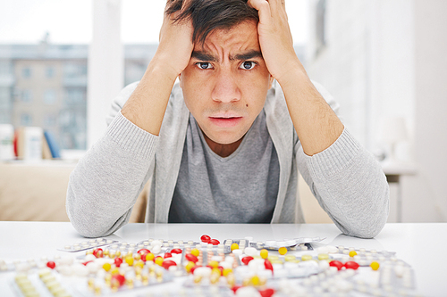Anxious young man  with assortment of tranquilizers near by