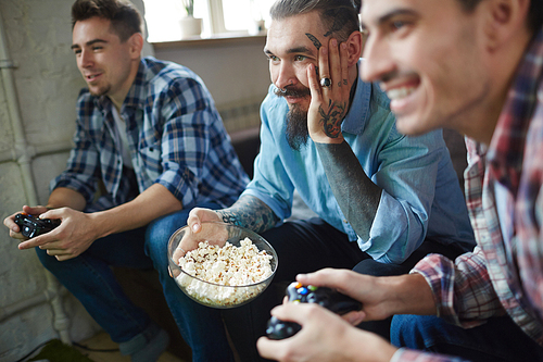 Bearded man with tattoos watching video game of his friends