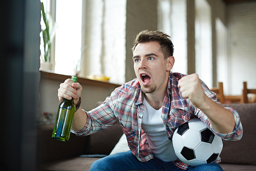 Excited football fan with beer and ball screaming in front of tv set