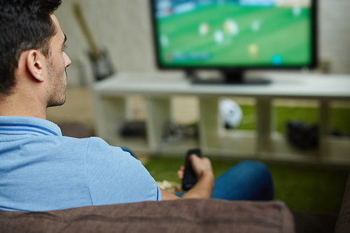 Young man with remote control sitting in front of tv set after work