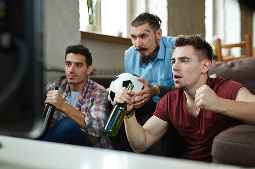 Young men with beer getting nervous while watching football match on tv