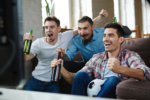 Ecstatic guys showing their gladness with triumph gesture in front of tv set