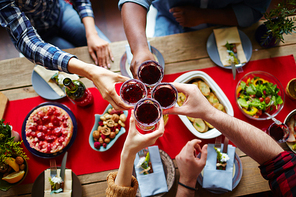 Group of friends toasting with glasses of red wine by festive table