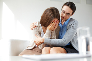 Lonely girl weeping while psychologist embracing her