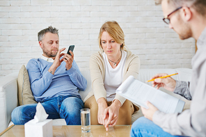 Desperate woman sharing her problem with psychologist while her husband browsing in smartphone by her side