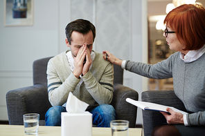 Upset man sitting in arm-chair during psychological session