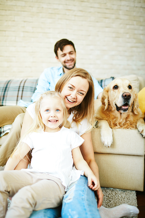 Happy female and little girl laughing on background of dog and young man relaxing on sofa