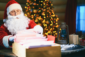 Concentrated Santa Claus sitting and checking his Christmas lists