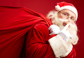 Santa with heavy sack showing shh gesture