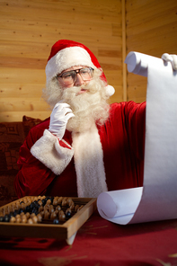 Santa Claus sitting at the table with abacus and checking his list