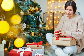 Pretty woman tying red ribbon on cover of gift-box