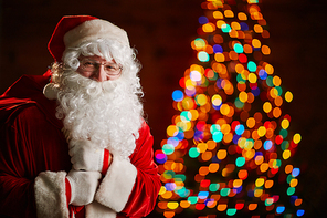 Happy Santa with sack of gifts on background of sparkling fir-tree