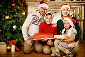 Happy family in Santa caps sitting by decorated Christmas tree