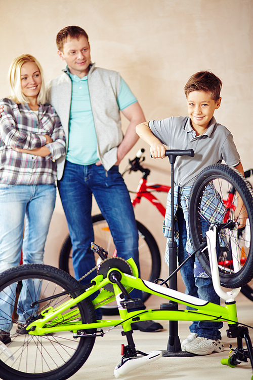 Cute boy repairing his bicycle himself with his parents standing behind