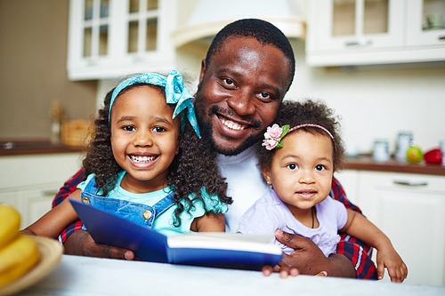 Smiling young father reading a book for his girls