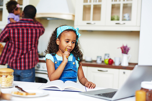 Little girl studying with book and laptop at home