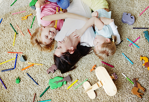 Happy mother lying on floor with her little daughters