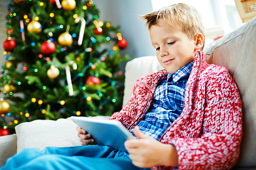 Little boy with touchpad sitting at home by Christmas tree