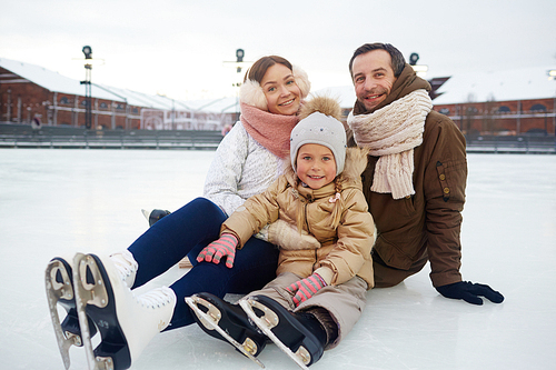 Urban family on skates sitting on ice of rink