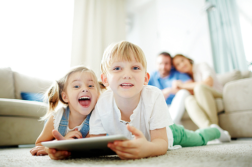 Happy siblings with touchpad lying on the floor