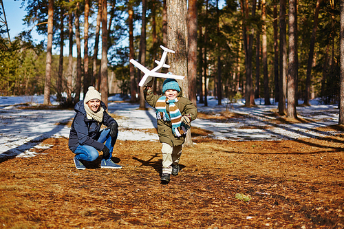 Carefree boy with toy plane running down forest path