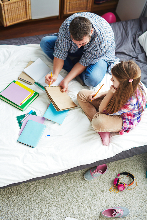 Man pointing at his drawing in notepad to teenage girl sitting near by