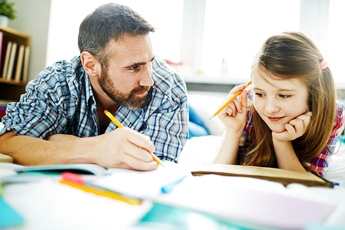 Cute girl looking at her father drawing and listening to his explanation