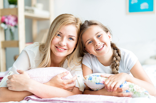 Adorable girl and young woman lying on bed at home