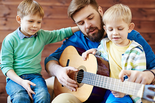 Young man showing his sons how to play guitar