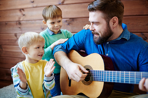 Young man playing guitar with two sons near by