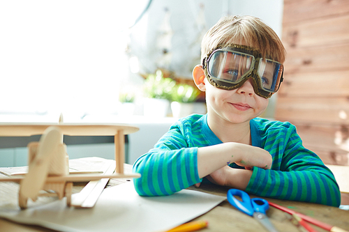 Cute boy in pilot goggles sitting by table