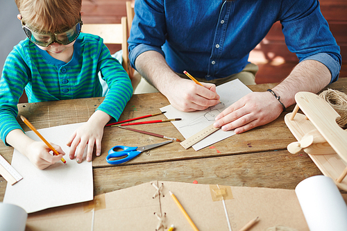 Cute boy in goggles drawing sketch with his father near by