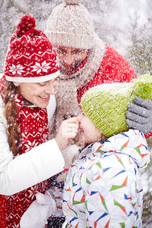 Happy woman playing with her laughing daughter in snowfall